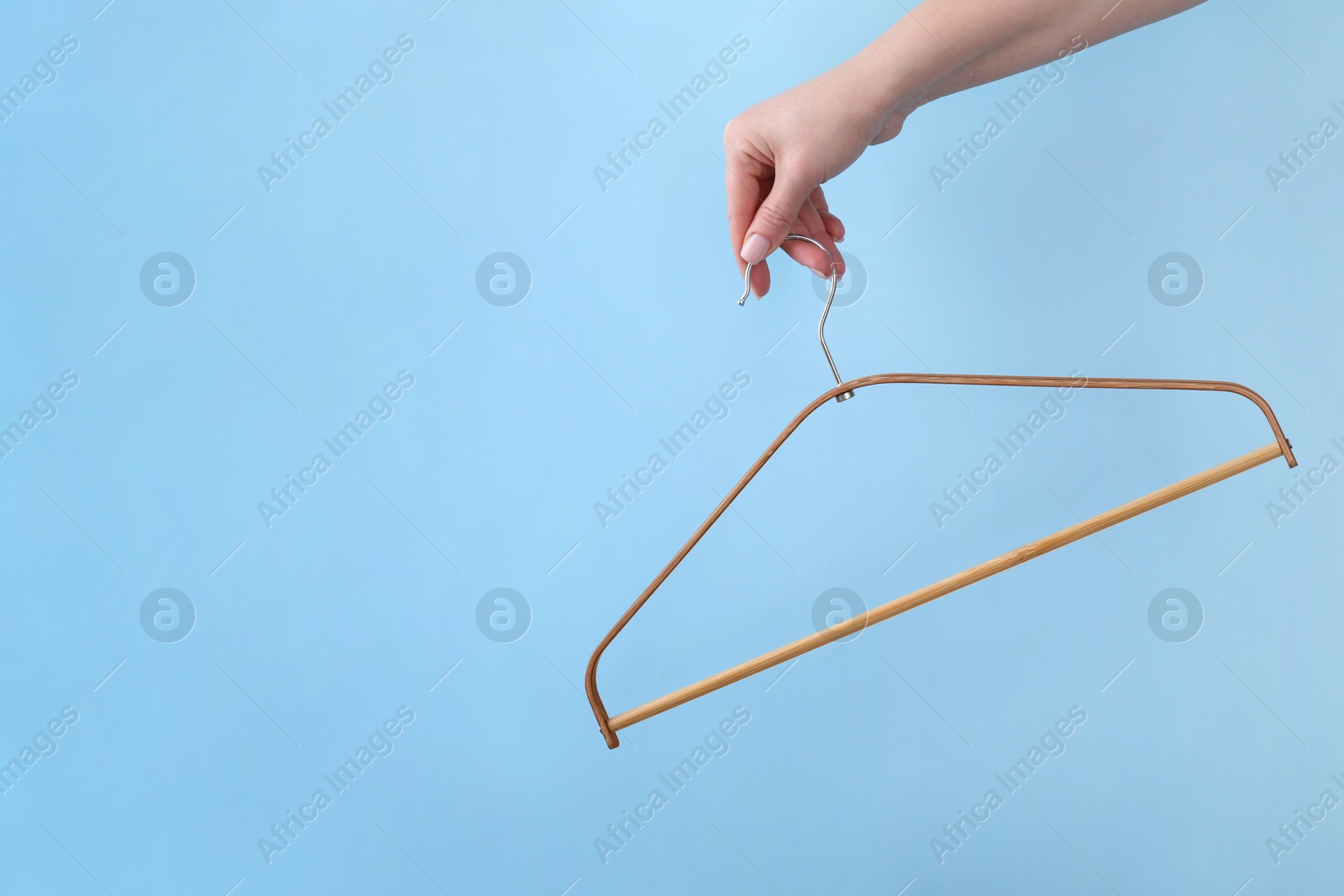 Photo of Woman holding hanger on light blue background, closeup. Space for text