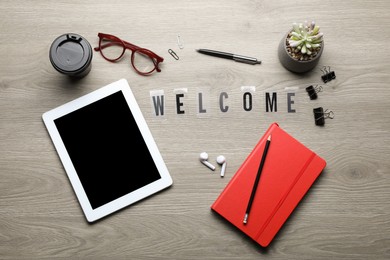 Flat lay composition with word Welcome, tablet and stationery on wooden table