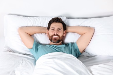 Photo of Happy man lying on comfortable pillows in bed at home