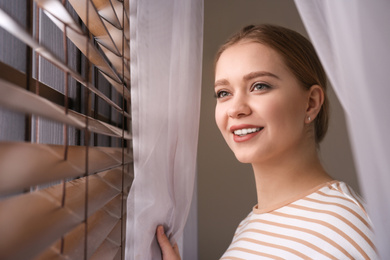 Woman near window with beautiful curtains at home