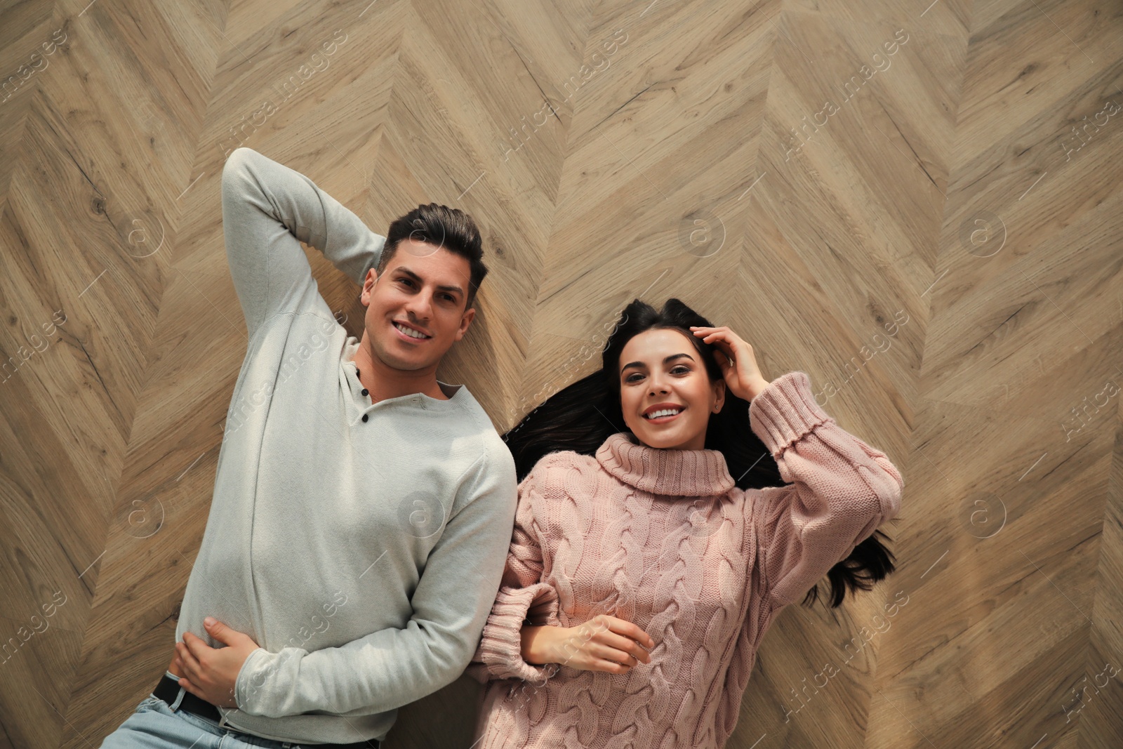 Photo of Happy couple lying on warm floor at home, top view. Heating system