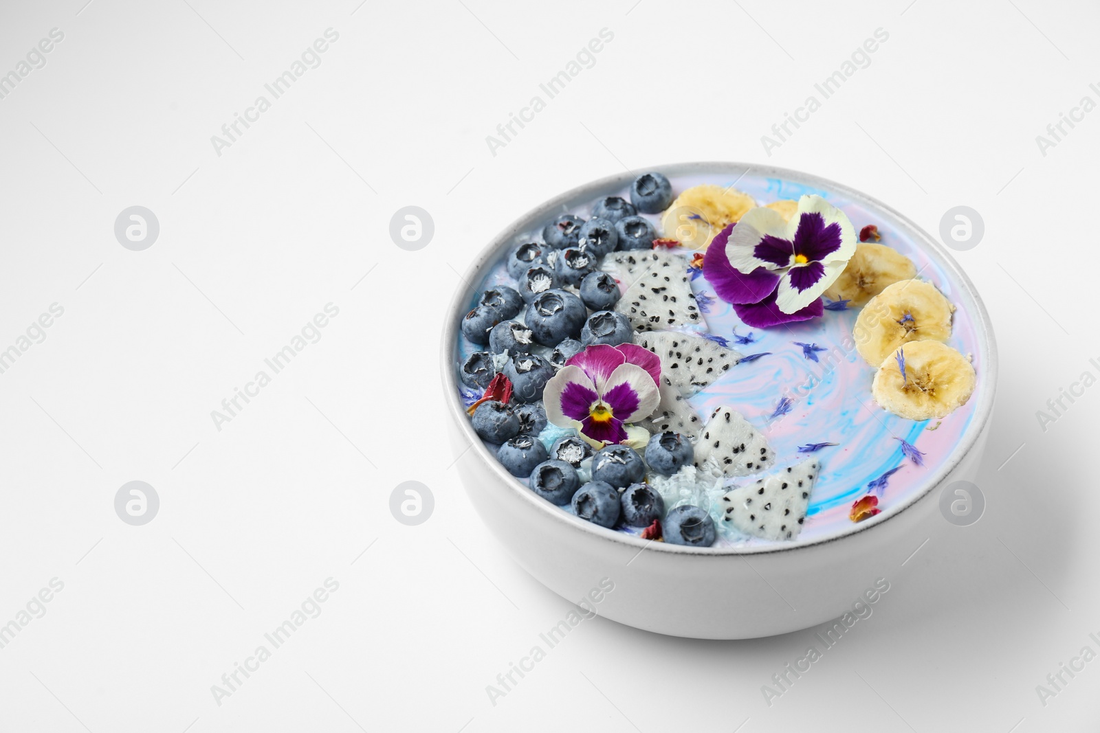 Photo of Delicious smoothie bowl with fresh fruits, blueberries and flowers on white background. Space for text