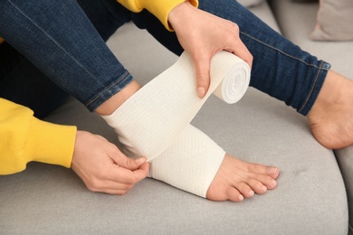 Photo of Young woman applying bandage on injured leg at home, closeup. First aid