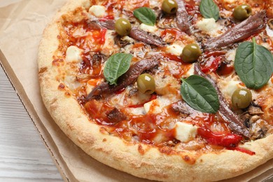 Photo of Tasty pizza with anchovies, basil and olives on white wooden table, closeup