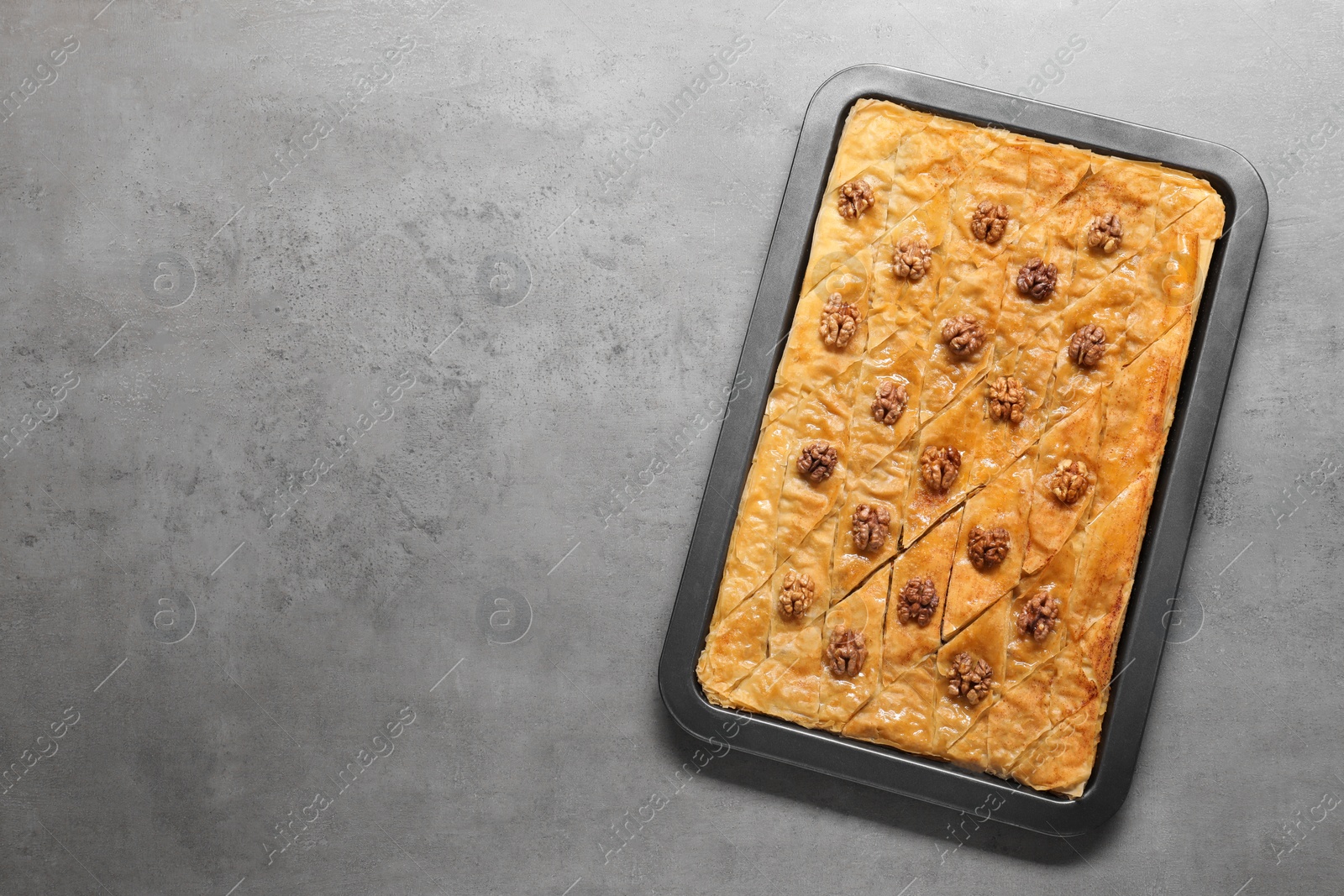 Photo of Delicious baklava with walnuts in baking pan on grey textured table, top view. Space for text