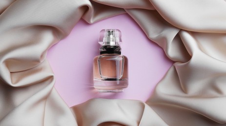 Photo of Luxurious bottle of perfume and beige silk on pink background, top view