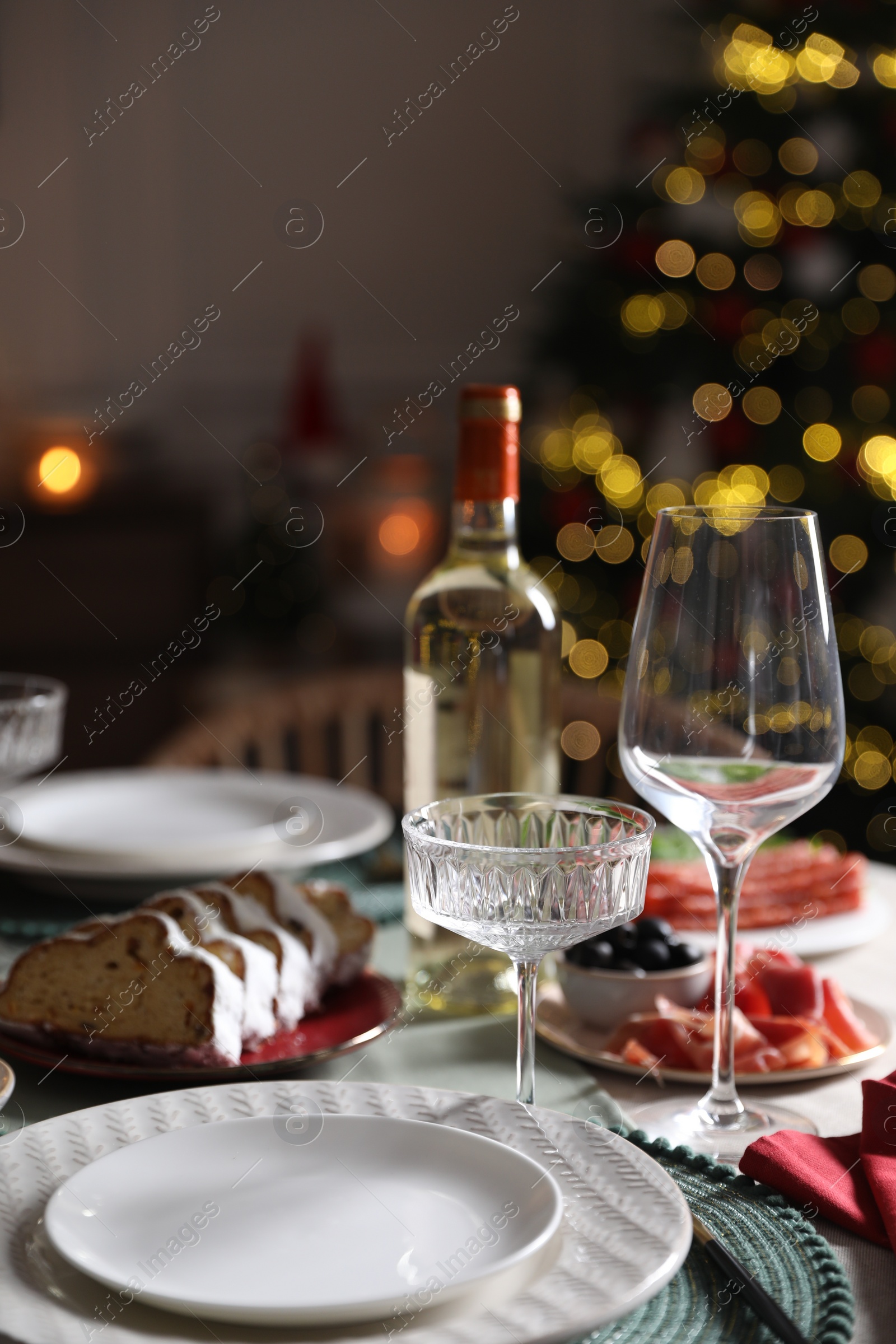 Photo of Christmas table setting with bottle of wine, appetizers and dishware indoors