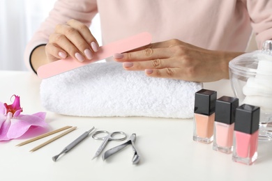 Woman filing nails covered with polish at table, closeup