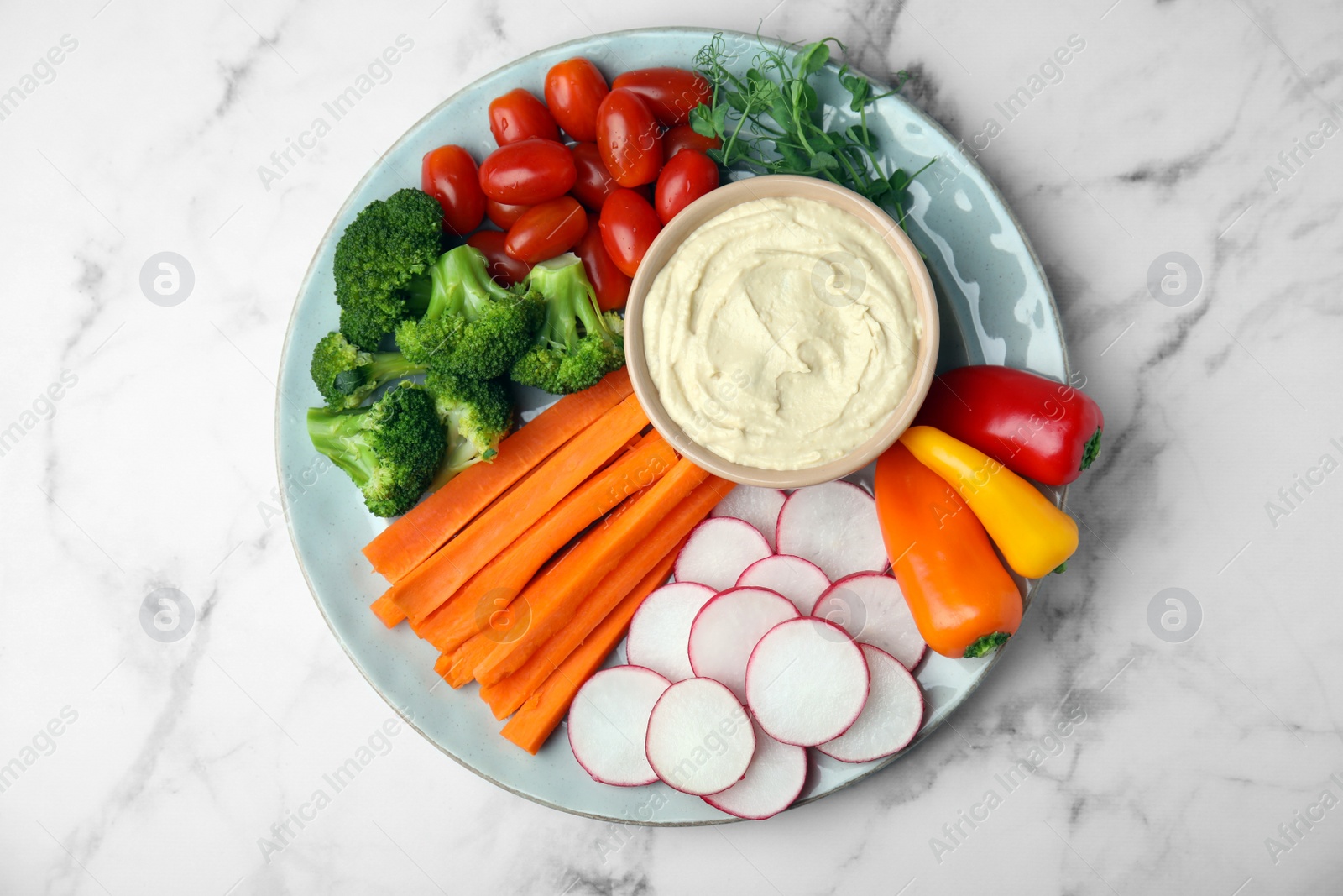Photo of Plate with delicious hummus and fresh vegetables on white marble table, top view