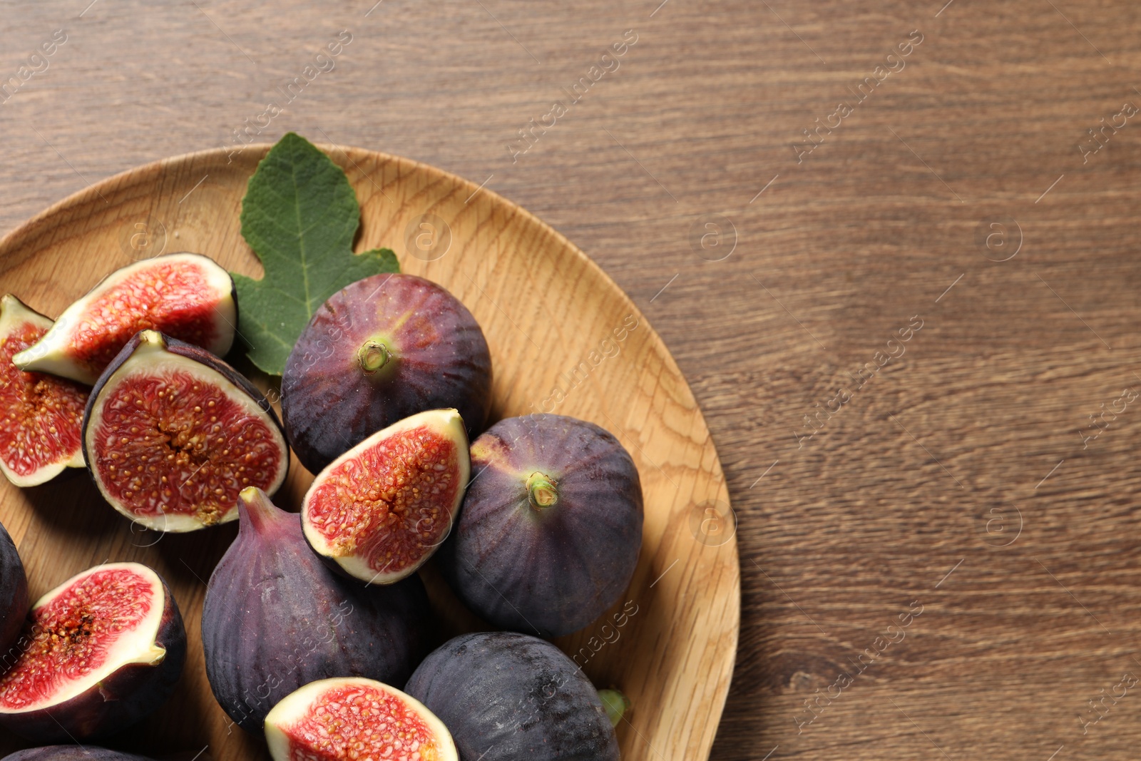 Photo of Whole and cut ripe figs with leaf on wooden table, top view. Space for text