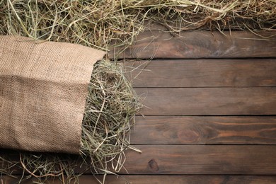 Photo of Burlap sack with dried hay on wooden table, top view. Space for text