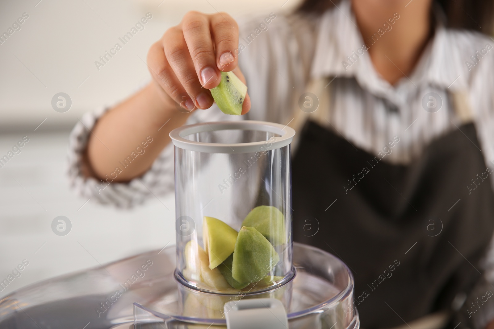 Photo of Young woman putting fresh kiwi into juicer in kitchen, closeup