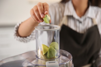 Young woman putting fresh kiwi into juicer in kitchen, closeup