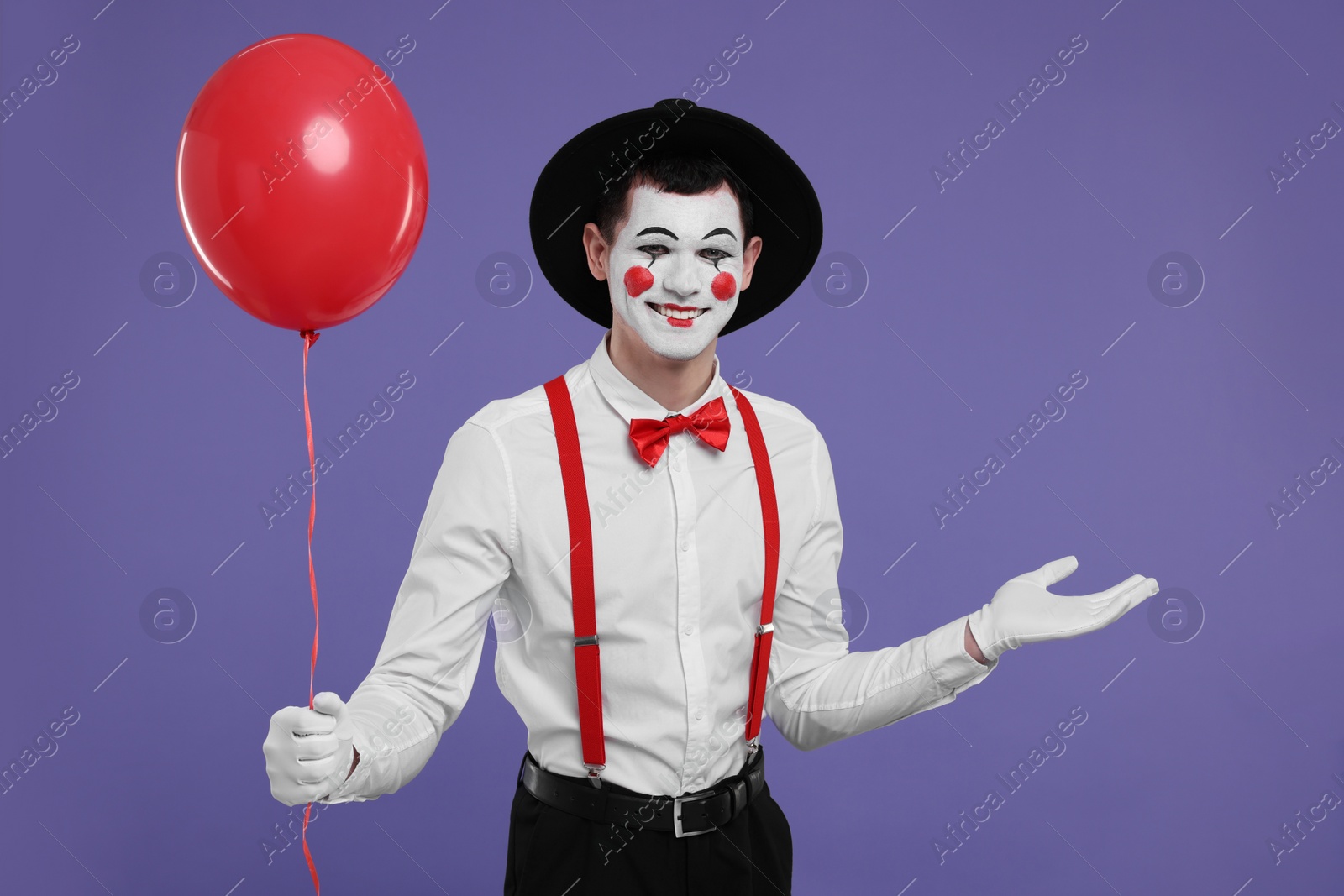 Photo of Funny mime artist with red balloon on purple background