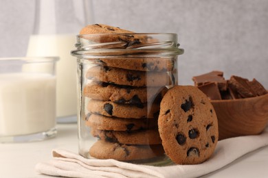 Glass jar with delicious chocolate chip cookies and milk on white marble table, closeup