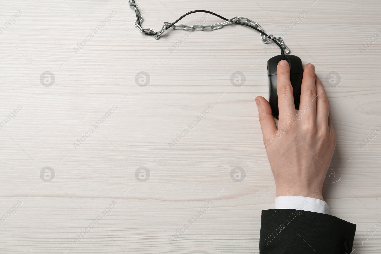 Photo of Top view of man using computer mouse at white wooden table, cable with chain. Internet addiction