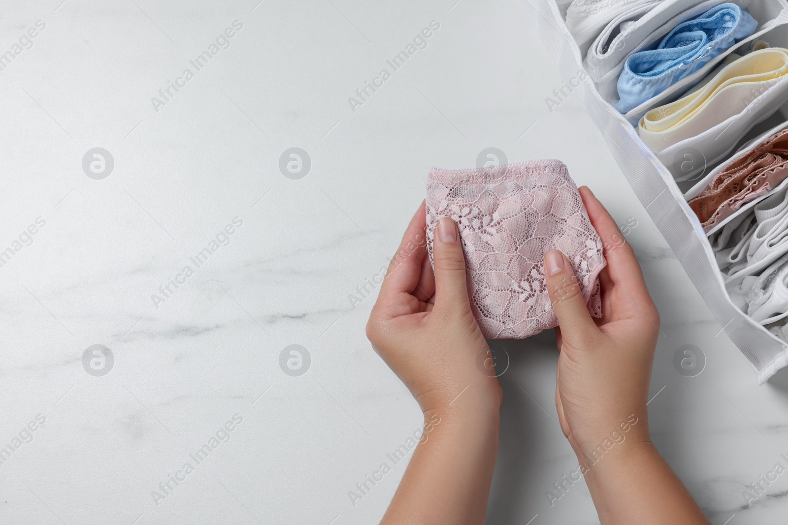 Photo of Woman with folded panties at white marble table with organizer of underwear, top view. Space for text