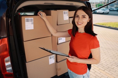 Courier with clipboard checking packages near delivery van outdoors