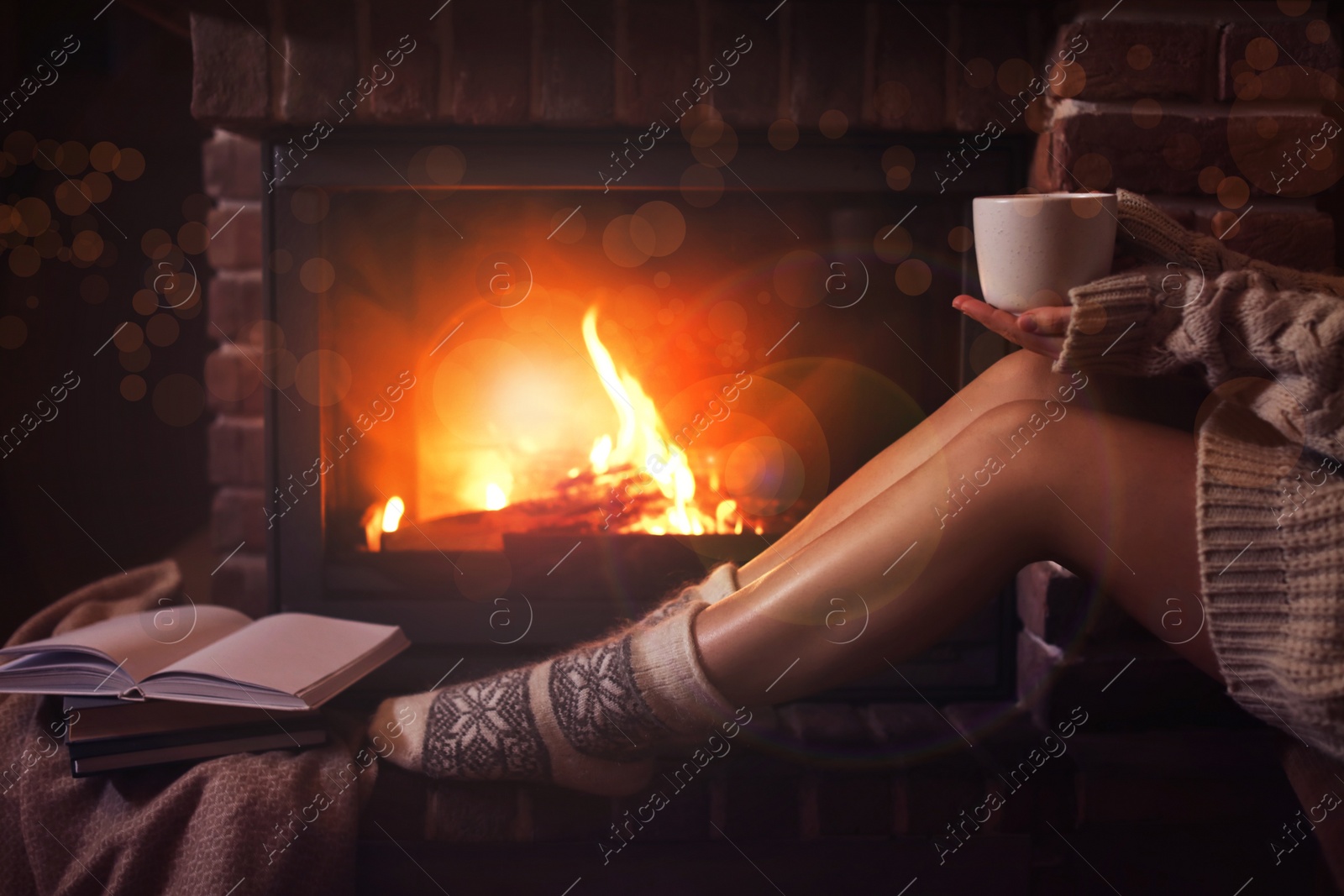 Image of Woman in knitted socks holding hot drink near fireplace at home, closeup. Winter vacation