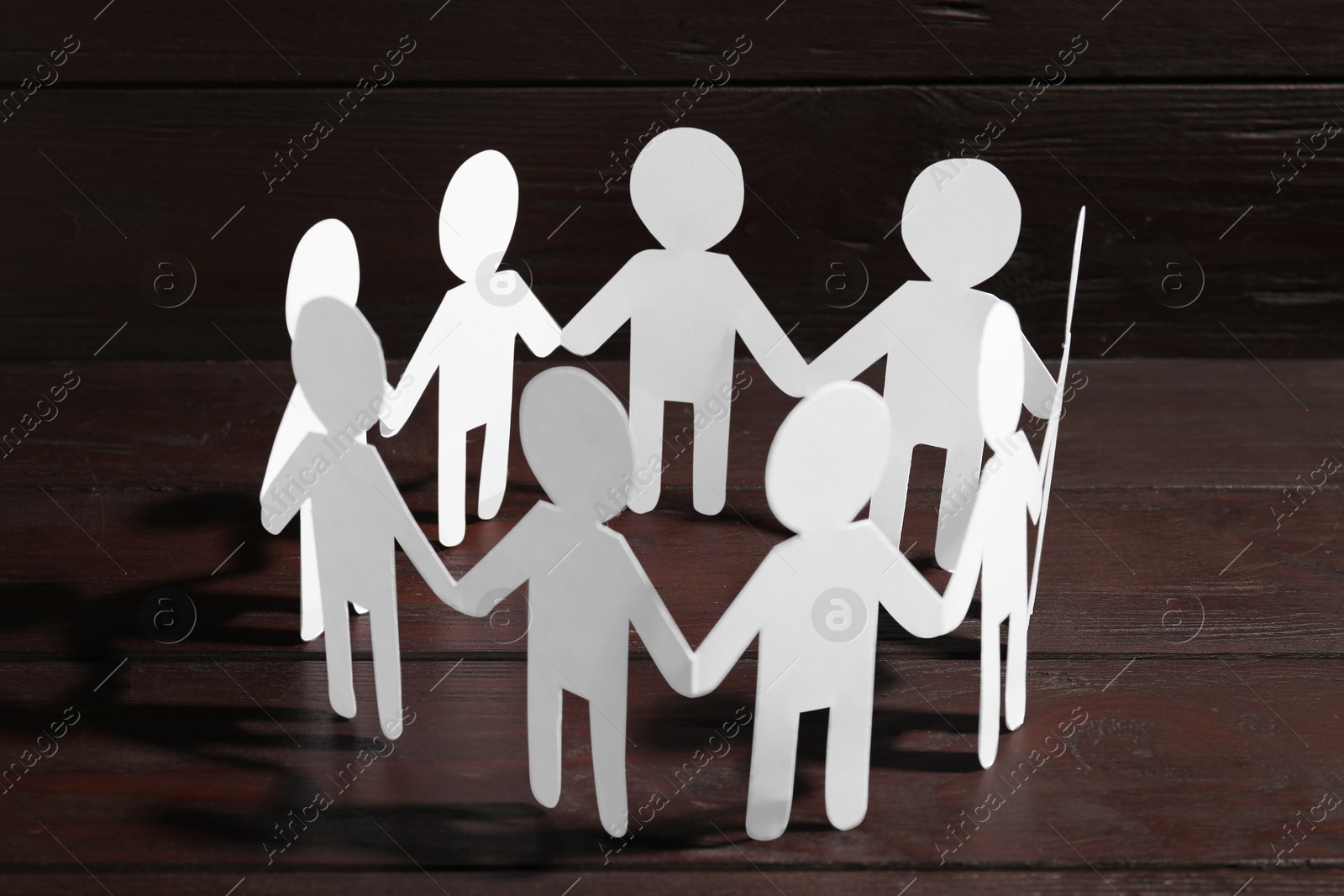 Photo of Teamwork concept. Paper figures of people holding hands on wooden table, closeup