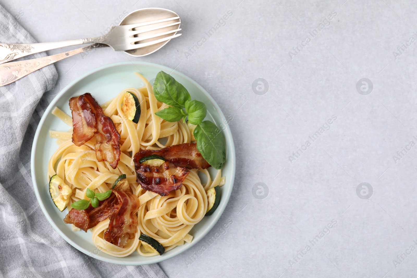 Photo of Tasty pasta with bacon and cutlery on light grey table, top view. Space for text