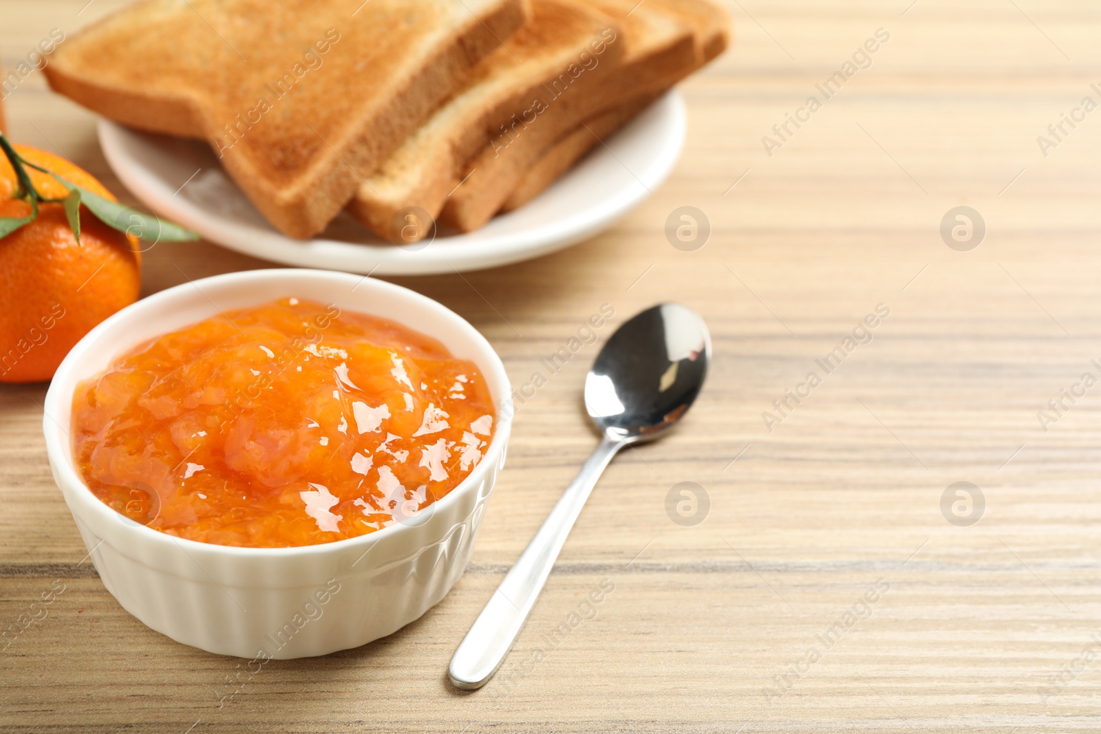 Photo of Tasty tangerine jam in bowl on wooden table. Space for text