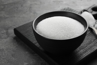 Photo of Granulated sugar in bowl on grey textured table, closeup. Space for text