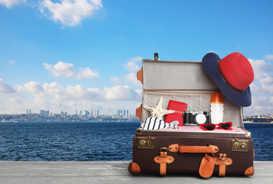 Image of Suitcase with different beach objects on grey wooden table near sea. Space for text