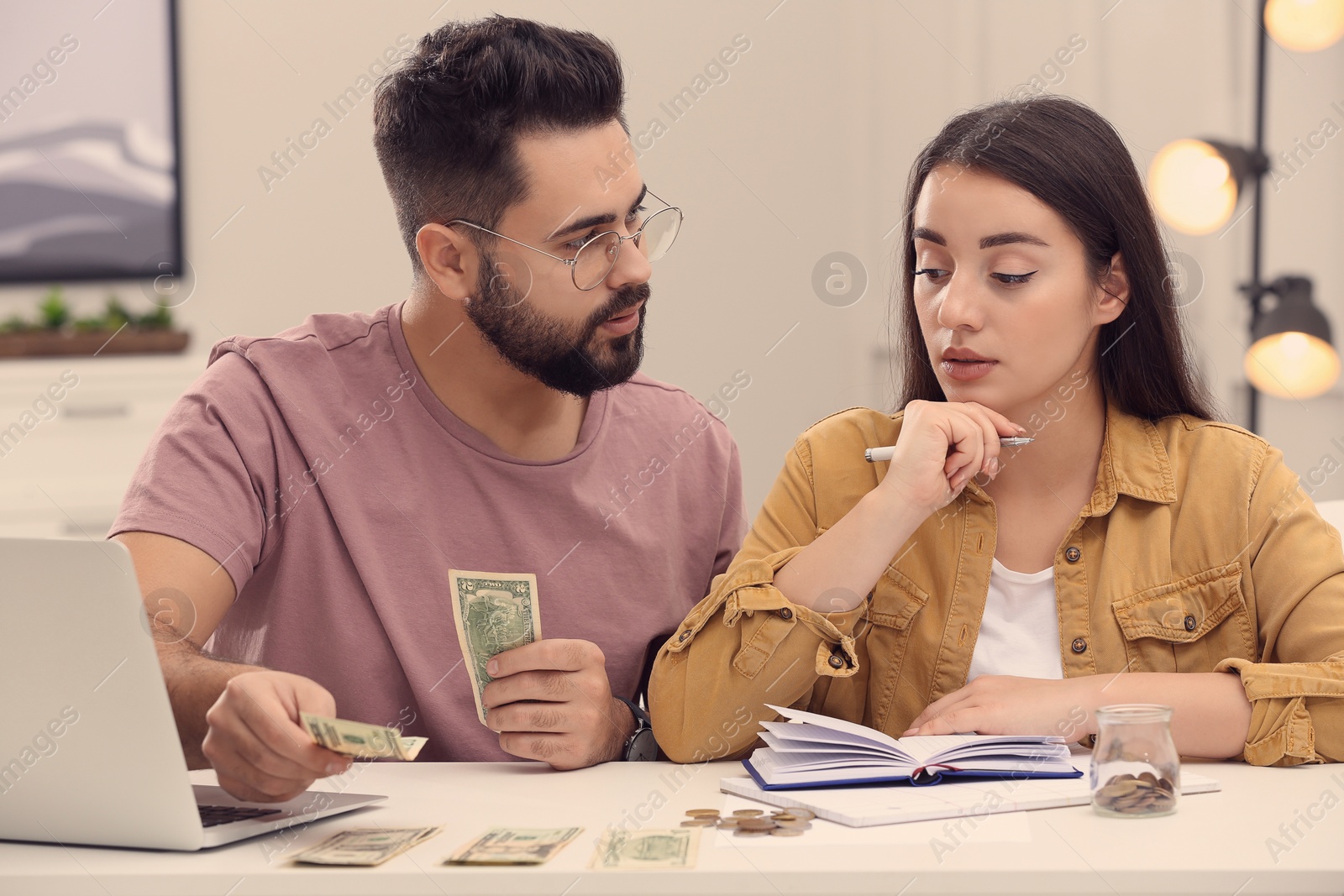 Photo of Young couple counting money at white table indoors