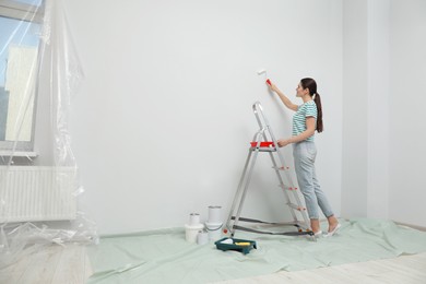 Photo of Woman near metallic folding ladder and painting wall indoors, space for text