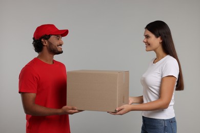 Photo of Smiling courier giving parcel to receiver on grey background