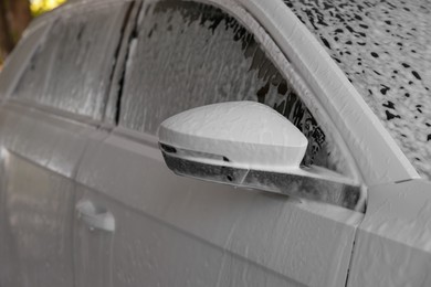 Photo of Auto covered with cleaning foam at outdoor car wash, closeup