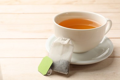 Photo of Tea bag and cup of hot beverage on light wooden table, closeup. Space for text