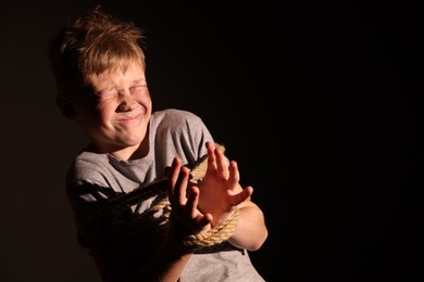 Photo of Scarred little boy with bruises tied up and taken hostage on dark background. Space for text