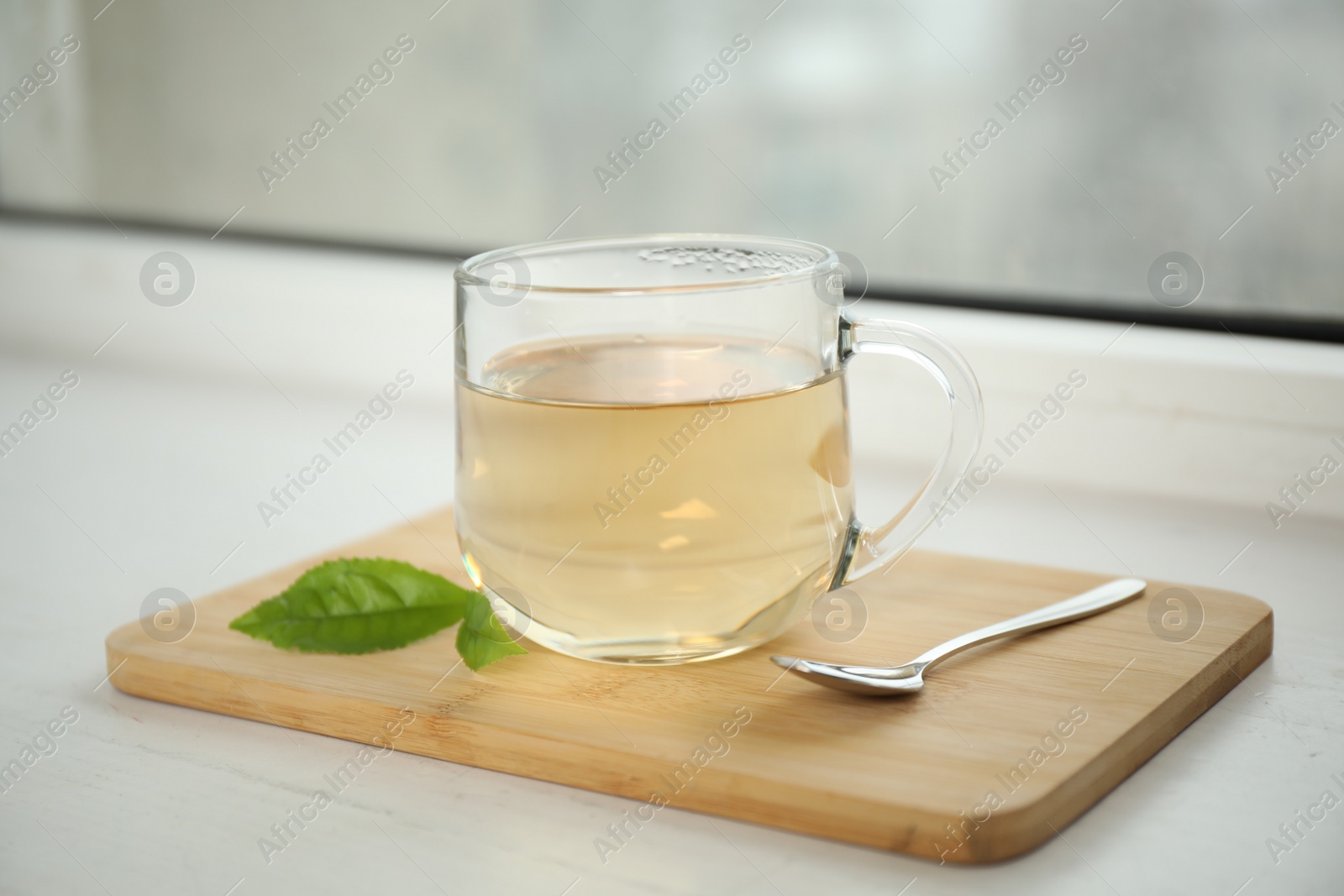 Photo of Tasty hot green tea in cup on window sill, closeup