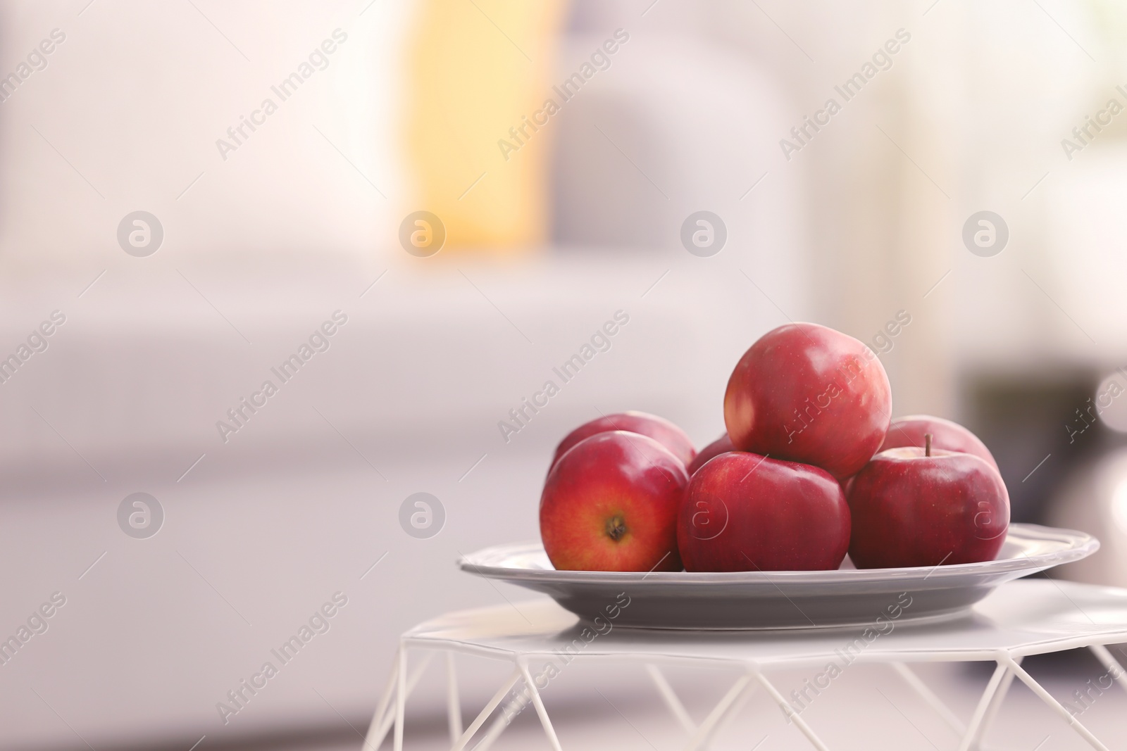 Photo of Plate with ripe red apples on table against blurred background