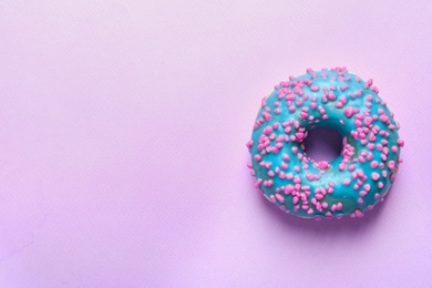 Delicious glazed doughnut with sprinkles on color background, top view