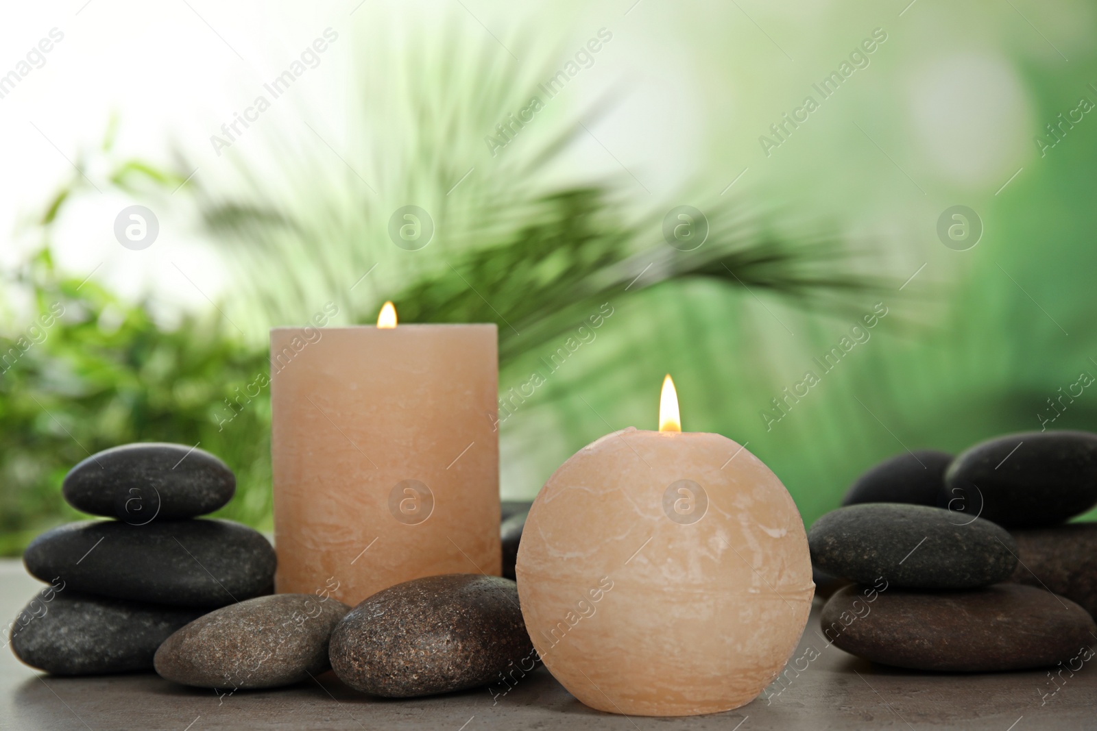 Photo of Burning candles and spa stones on table against blurred green background