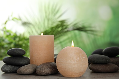 Photo of Burning candles and spa stones on table against blurred green background