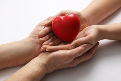 Photo of Young and elderly women holding red heart on white background, closeup