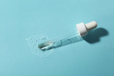 Pipette with cosmetic serum on light blue background, top view