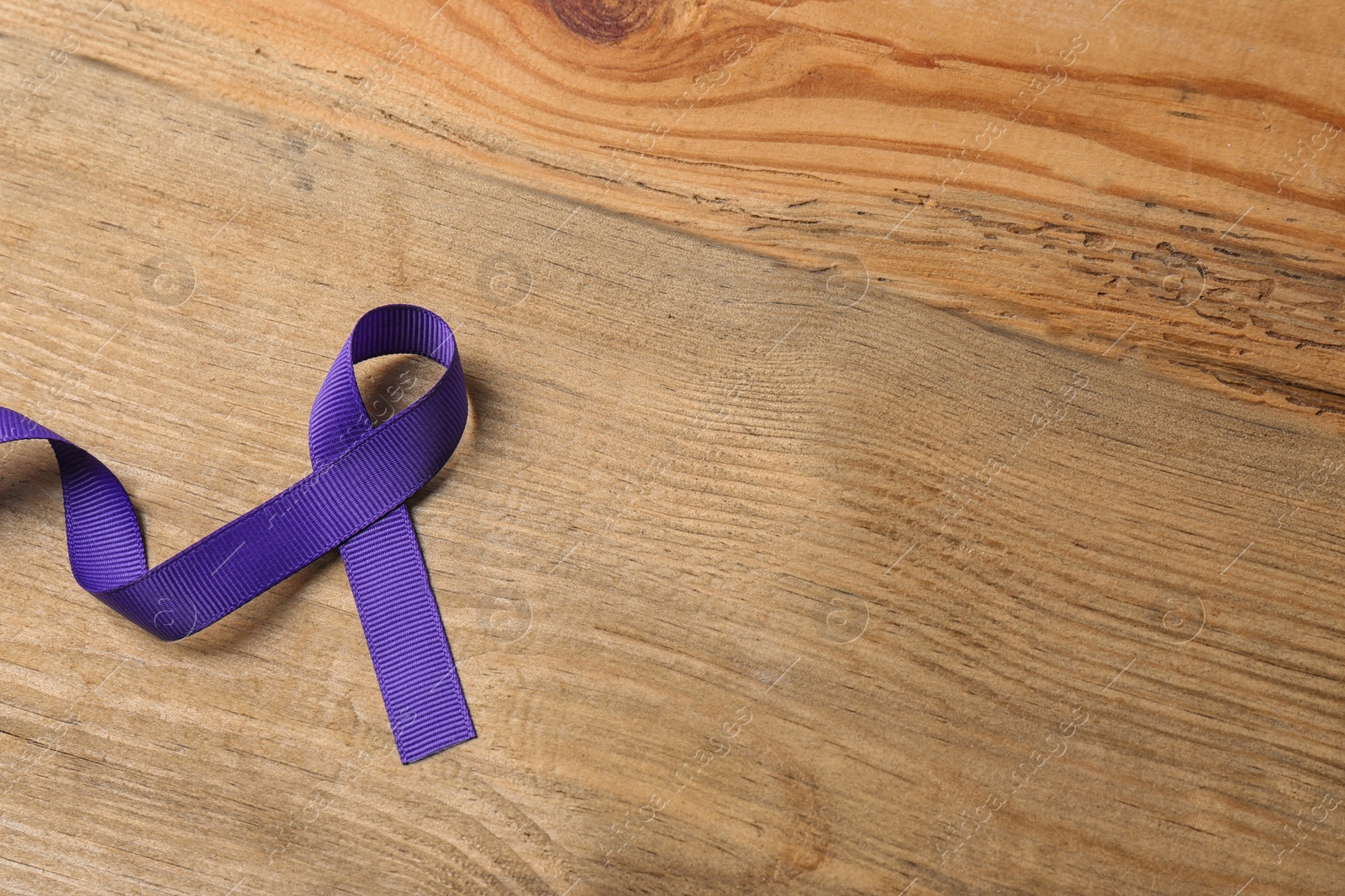 Photo of Purple ribbon on brown wooden background, space for text. Domestic violence awareness