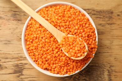 Photo of Raw red lentils in bowl and spoon on wooden table, top view