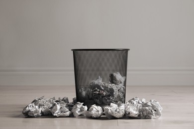 Photo of Metal bin with crumpled paper near white wall indoors. Rubbish recycling