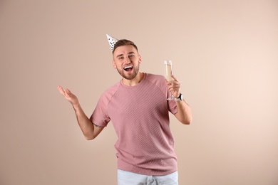 Portrait of happy man with party cap and champagne in glass on color background