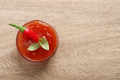 Spicy chili sauce with basil on wooden table, top view. Space for text