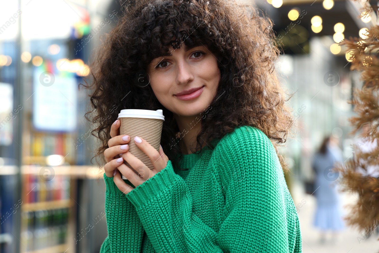 Photo of Young woman in stylish green sweater with cup of coffee outdoors