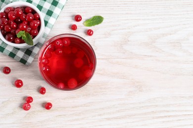 Photo of Tasty cranberry juice in glass and fresh berries on white wooden table, flat lay. Space for text