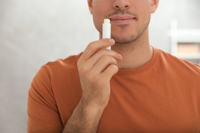 Photo of Man applying hygienic lip balm indoors, closeup