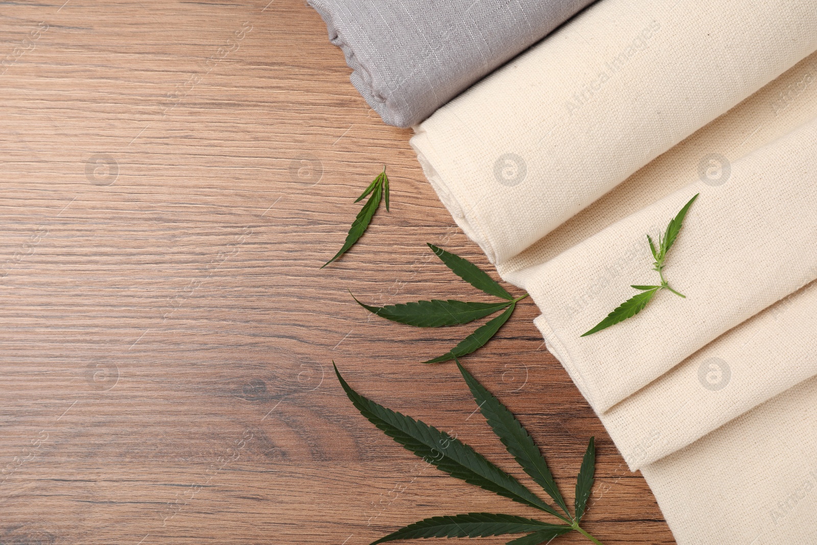 Photo of Hemp cloths and green leaves on wooden table, flat lay. Space for text